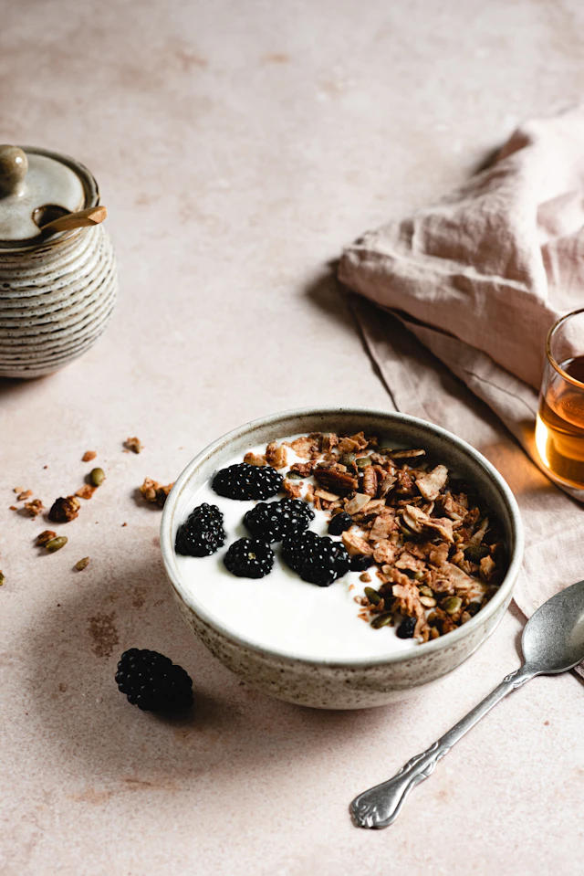 Yogurt with blackberries and granola beside a teapot and a cup of tea.